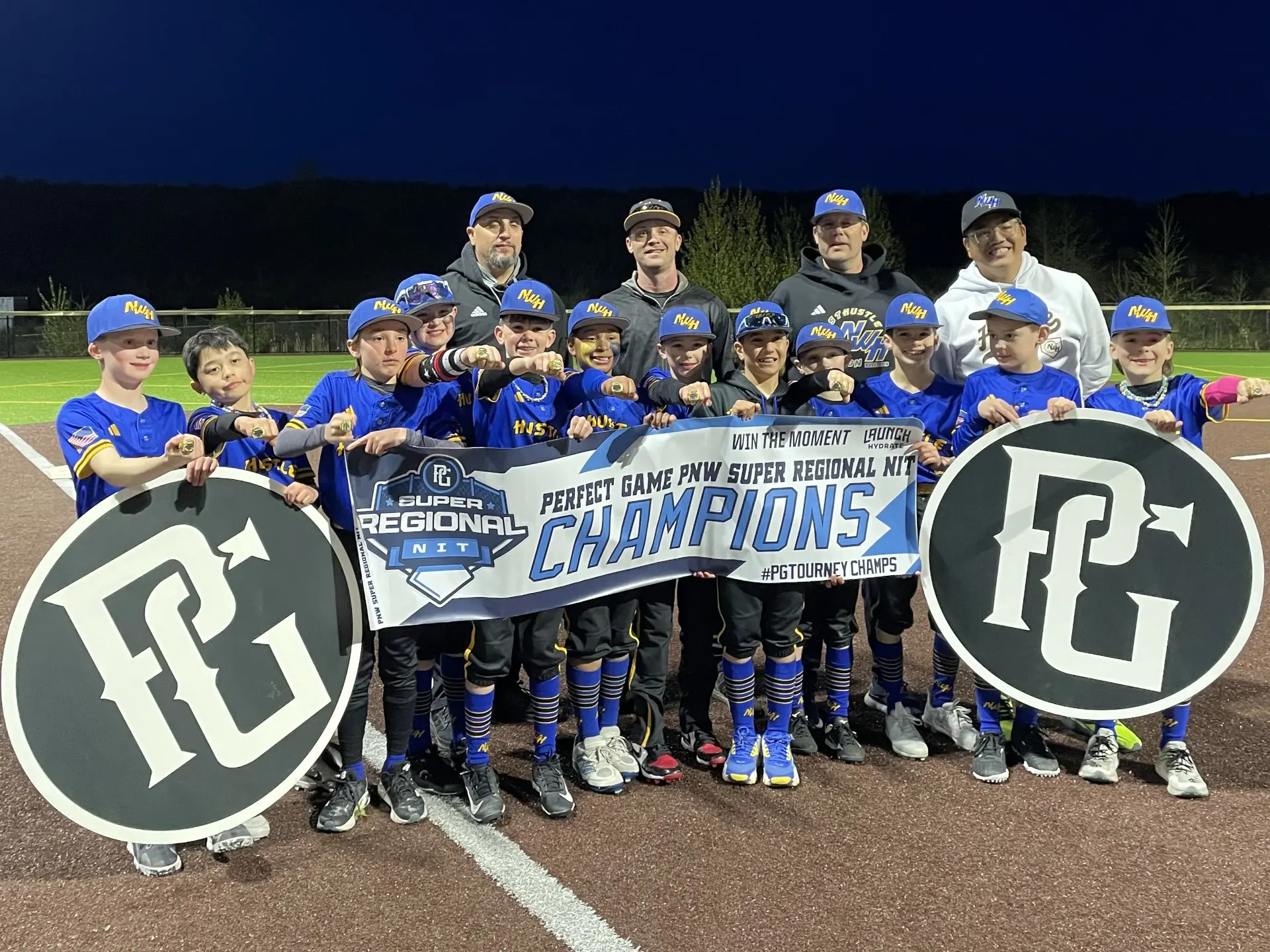 Northwest Hustle youth baseball team celebrating a championship victory with a banner and rings.